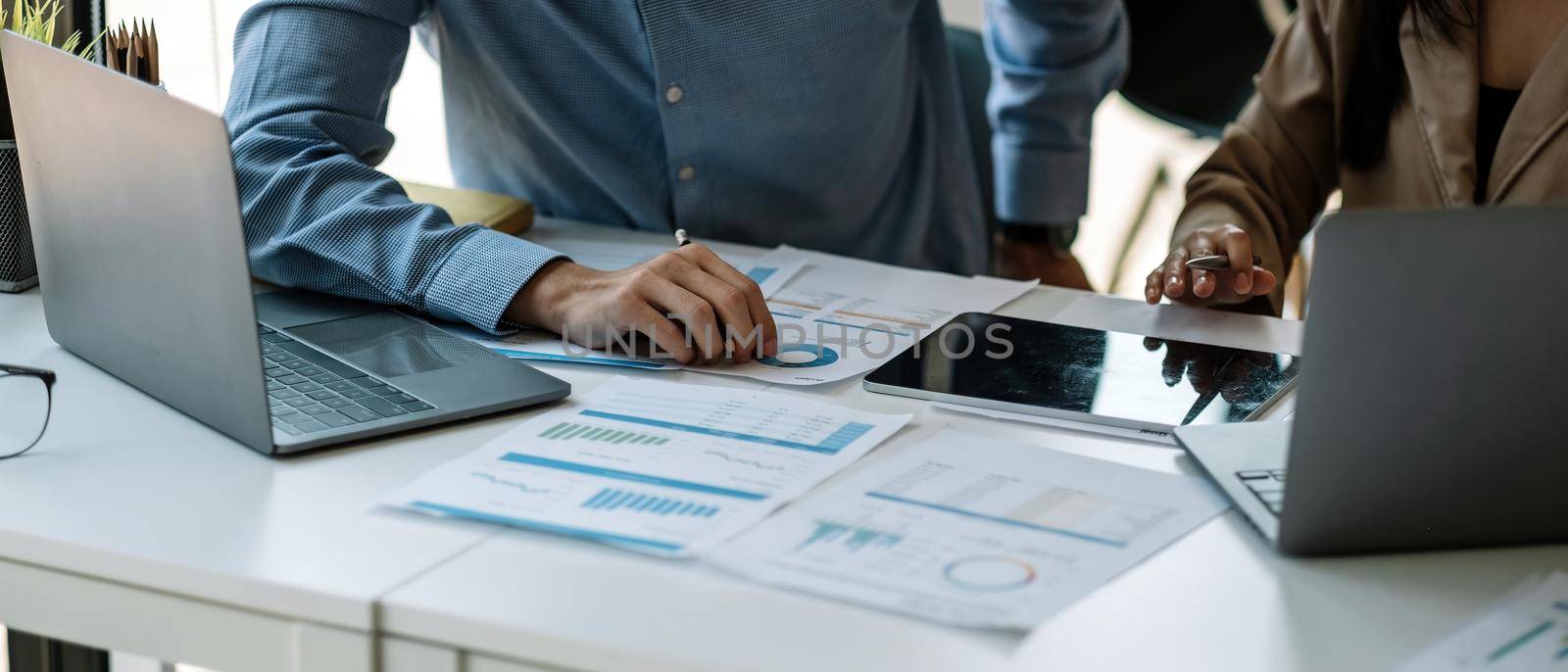 businessman and partnership pointing the graph to analyze the marketing plan with calculater and laptop computer on wood desk in office by nateemee