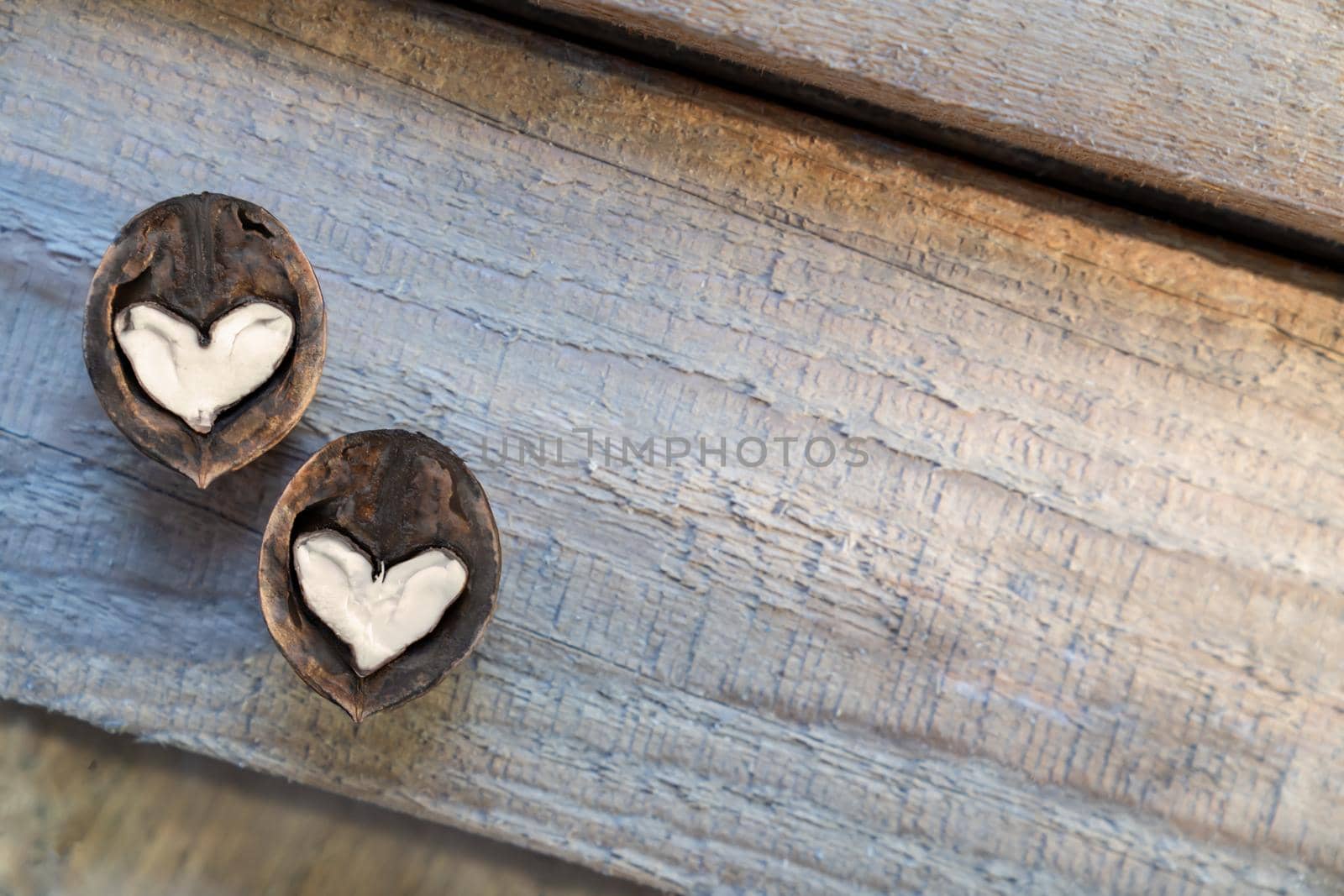 Two halves of split walnut with core in form of white hearts on wooden background, diagonal lines. Concept of Valentine's Day and health. by Laguna781