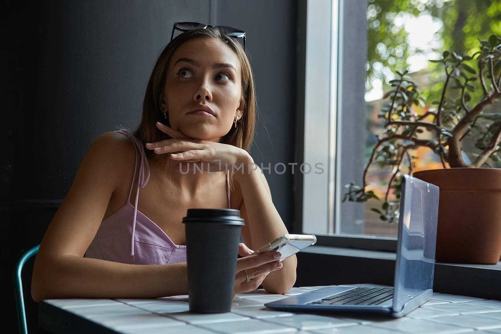 young asian woman sitting at table near window, using her smartphone. beautiful lady surfing internet on cell phone at cafe, chatting online. modern communication technology, distant work, remote job