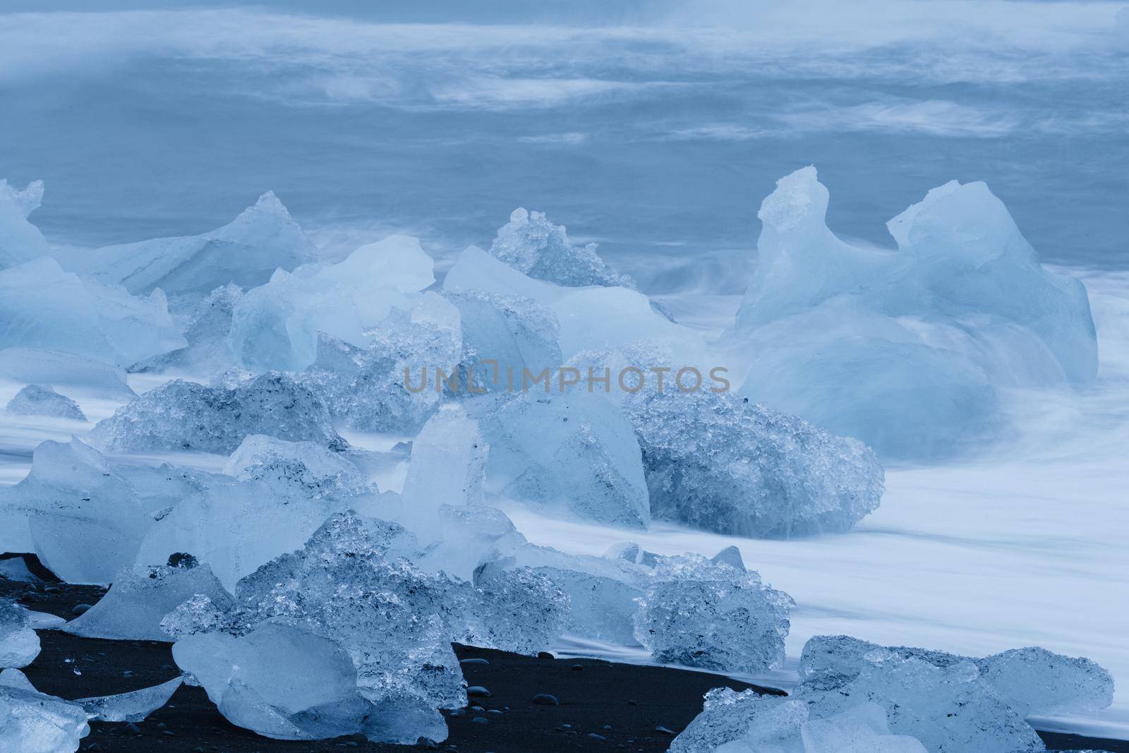 Spectacular icebergs over the black sand beach beaten by the breaking waves, long exposure