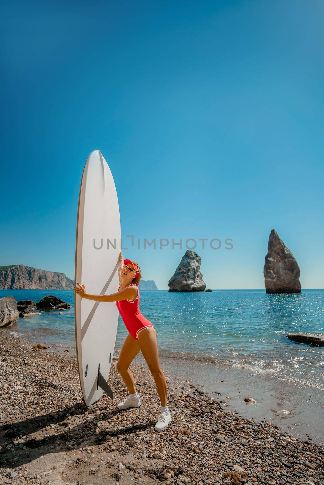 Woman surfer during summer travel to beach vacation. A middle-aged woman in a red swimsuit and a cap with sap on the background of the sea and rocks in the water. extreme sport. Travel, weekend, lifestyle