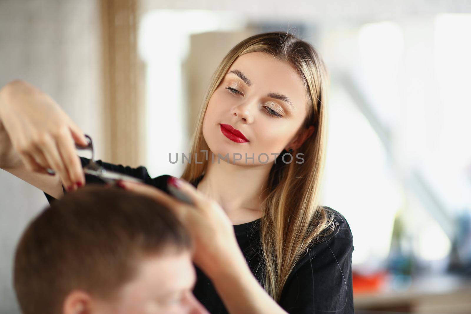 A beautiful girl cuts a man's hair with scissors, close-up. Hairdressing services, men's haircut, beauty salon