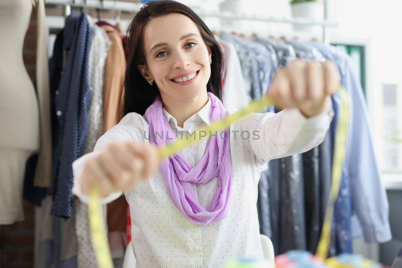 Designer, seamstress in the atelier shows a measuring tape, close-up, blurry. Designing and creating outfits