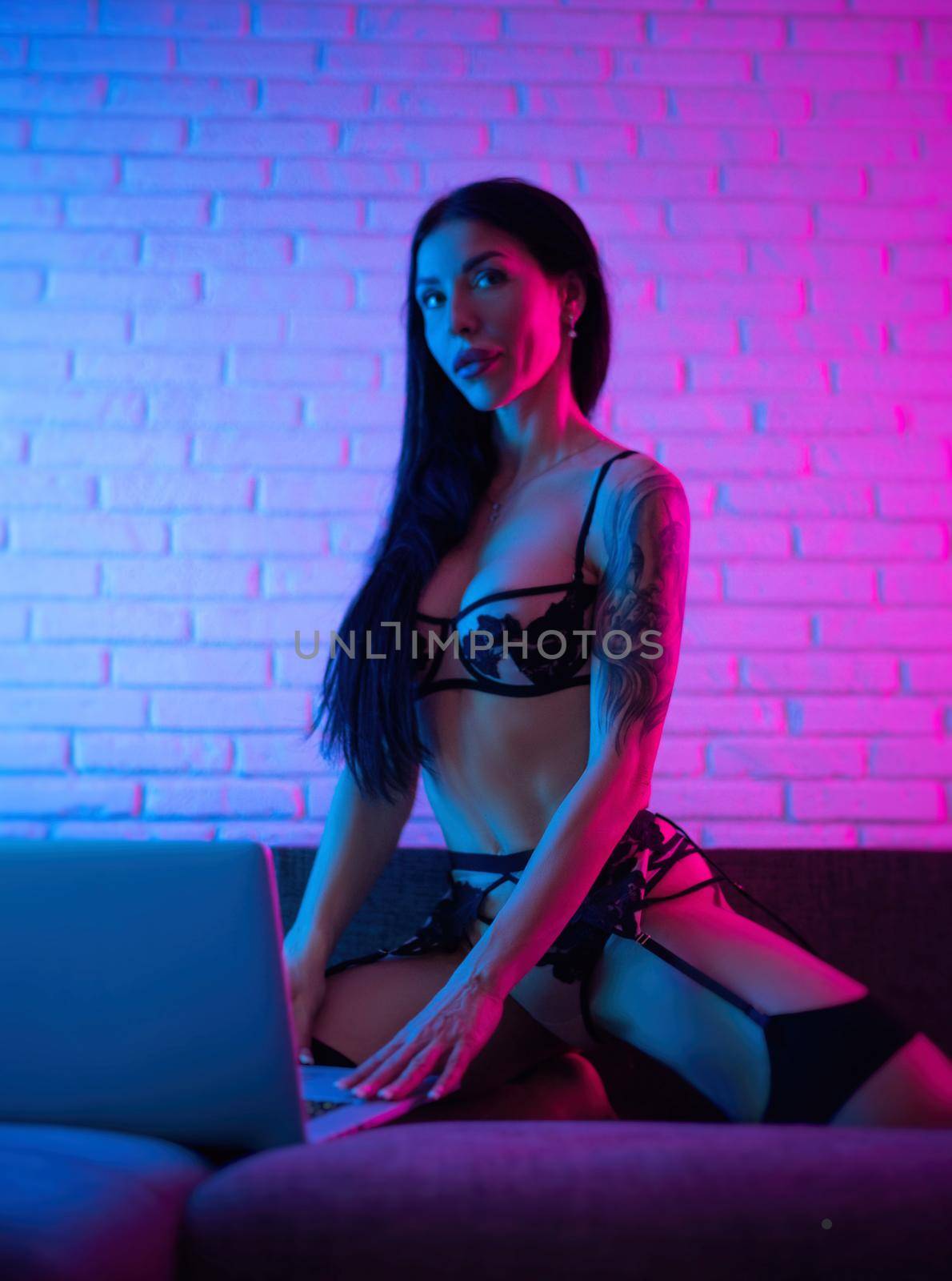 adult woman in sexy underwear in neon light on sofa with laptop by Rotozey