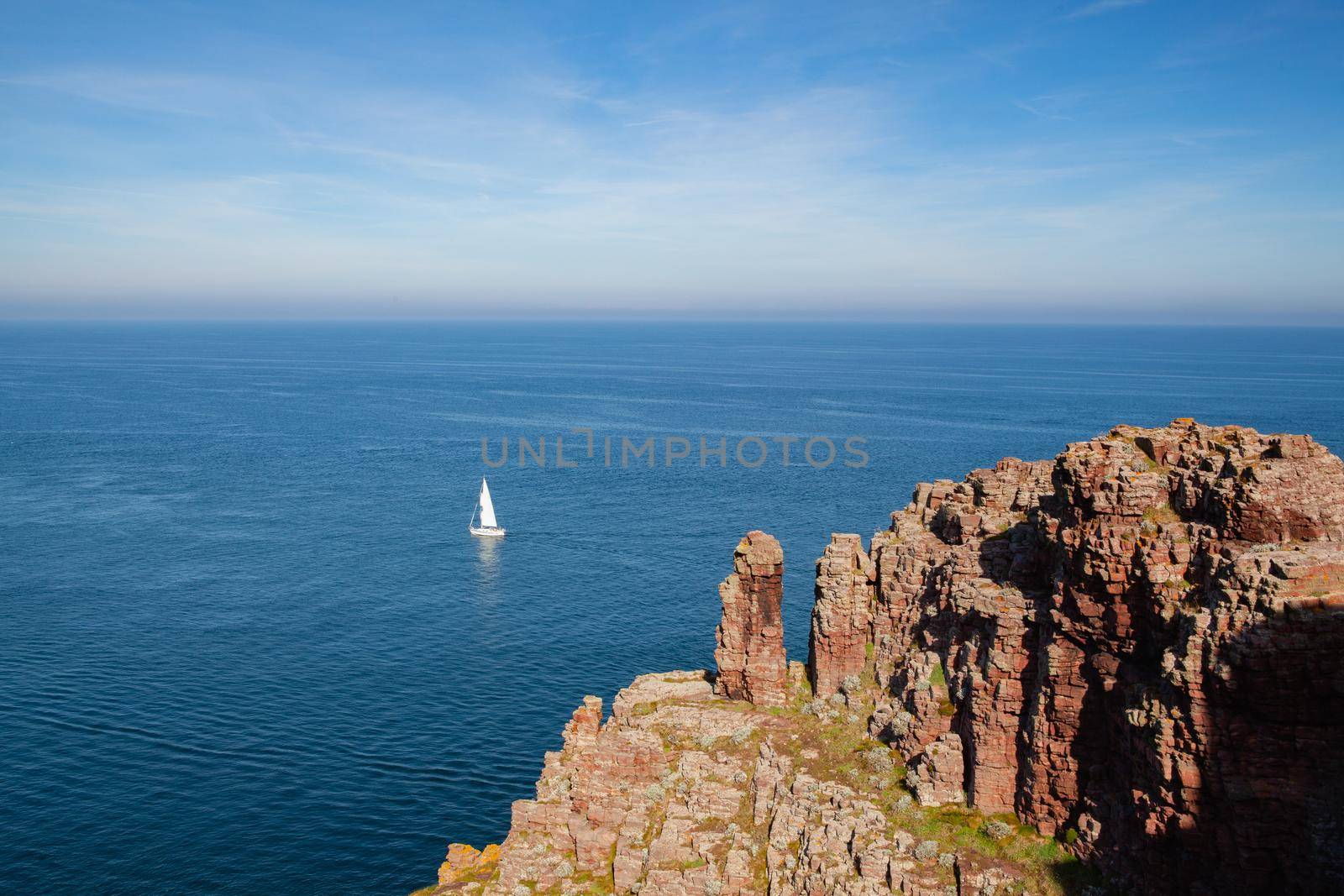 Lonely sailboat on the sea next to Cap Frehel. Cap Frehel is a peninsula in Cotes-d Armor, in northern Brittany, France. Lighthouse Cap Frehel, standing 60m on a rock above the sea