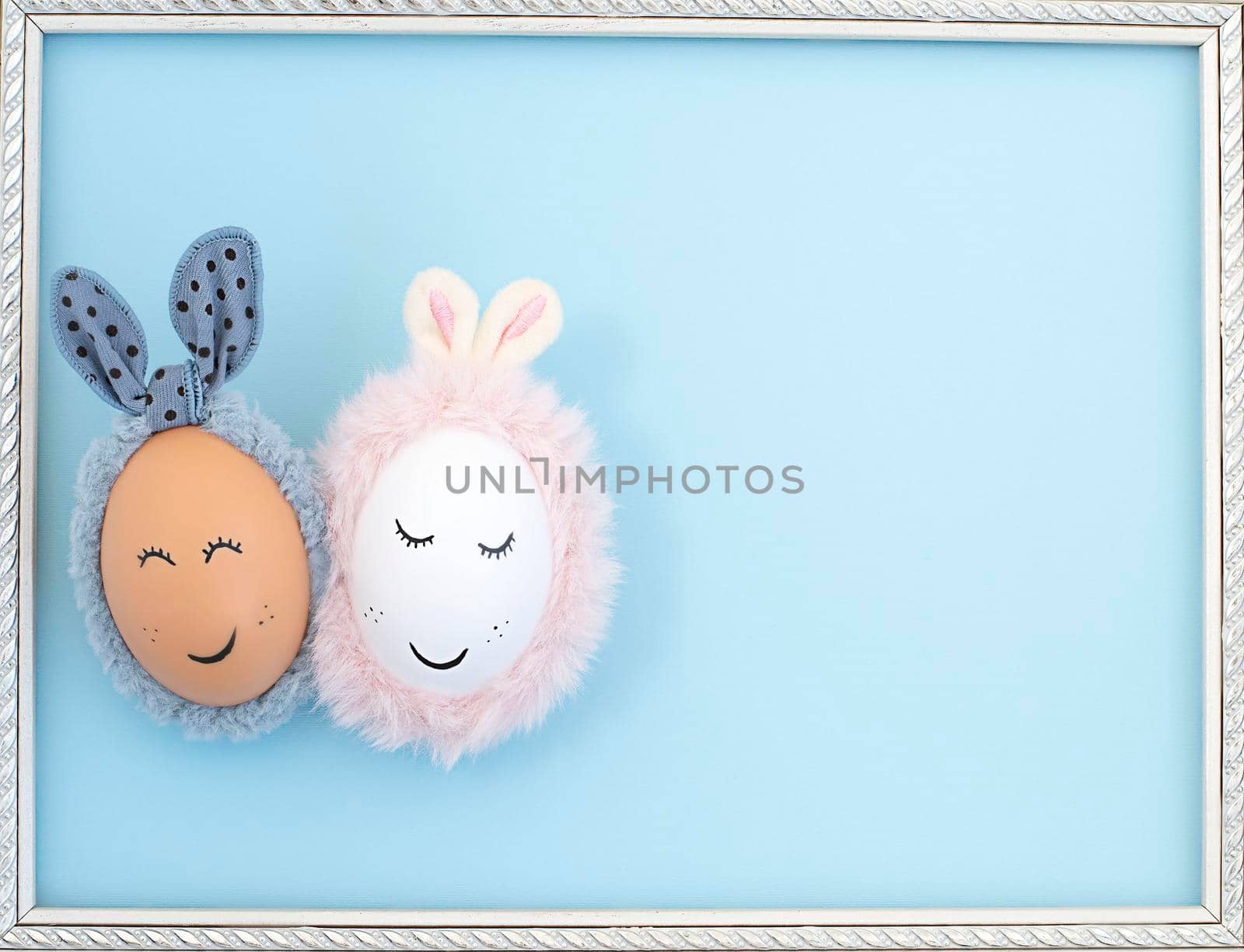 Two Easter eggs with painted eyes and rabbit ears on a blue background in a white frame. close up