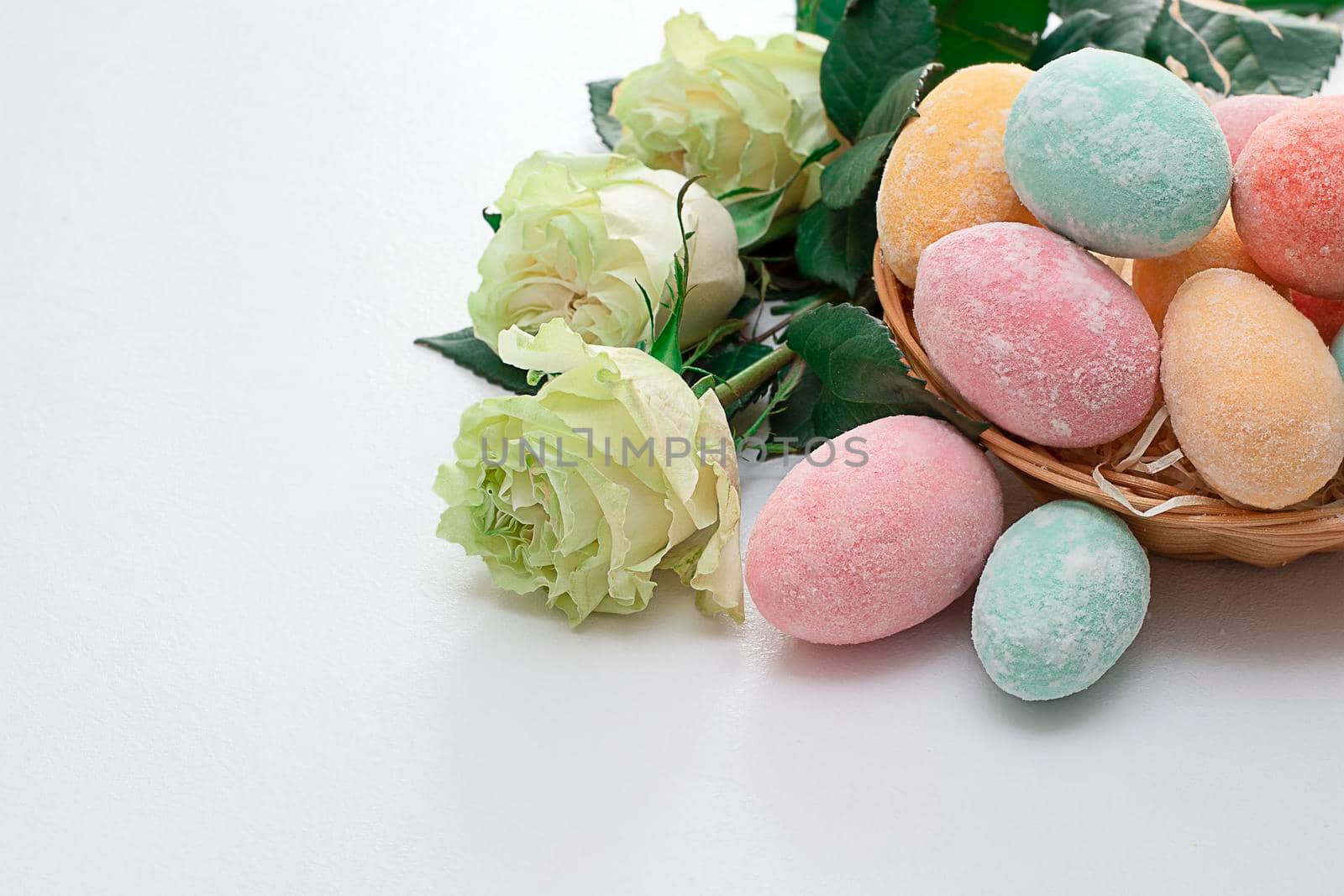 Easter composition. Easter colorful eggs in a wicker basket and roses on a white table. Soft focus. copy space by ketlit