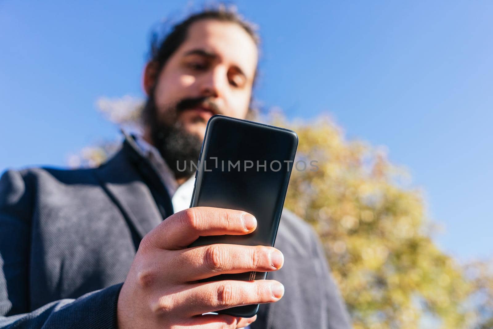 young business man looking phone near to office. Natural light in a sunny day.