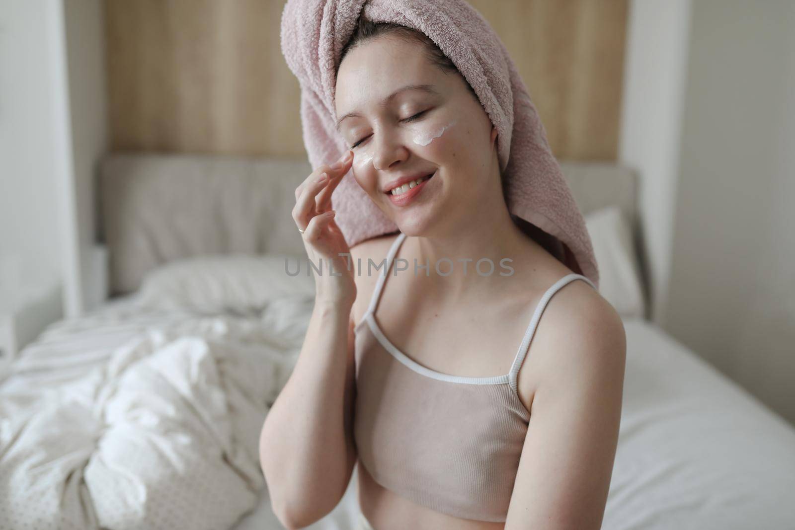 beauty, skin care, spa concept, smiling young woman with a towel on head apply cream on face skin
