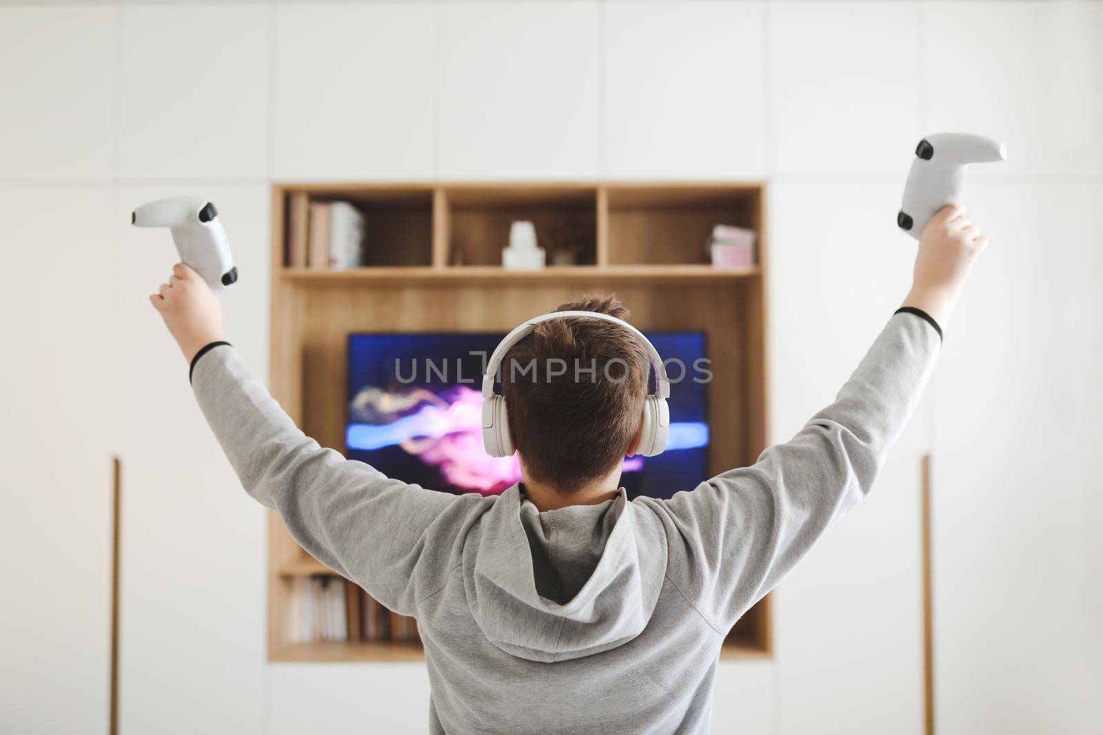 Boy in headphones watching television, teenager boy playing video game in front of screen at home.