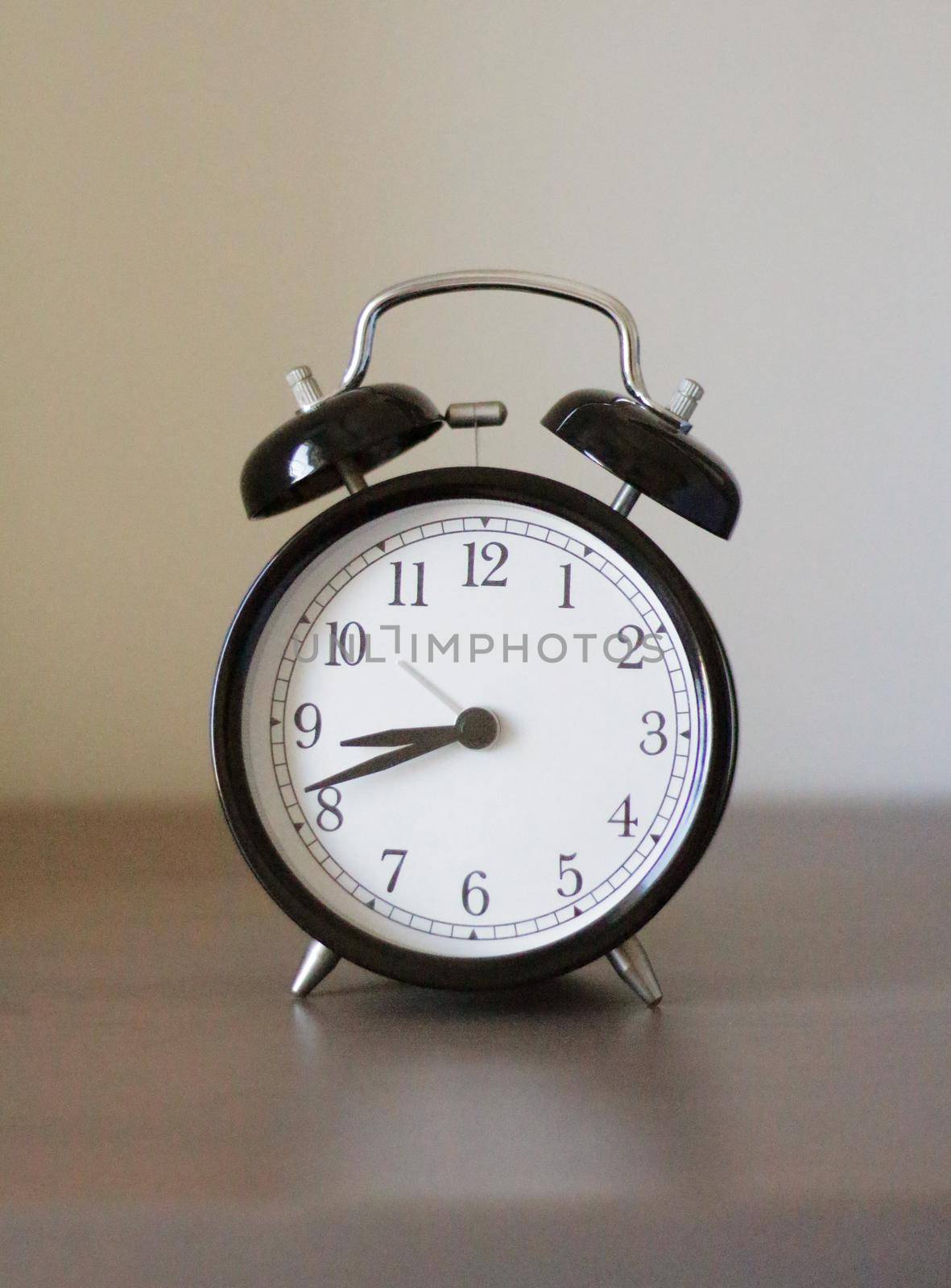 On an old alarm clock, the time is 8:40 am. It's time to wake up. Alarm clock is on a wooden table.