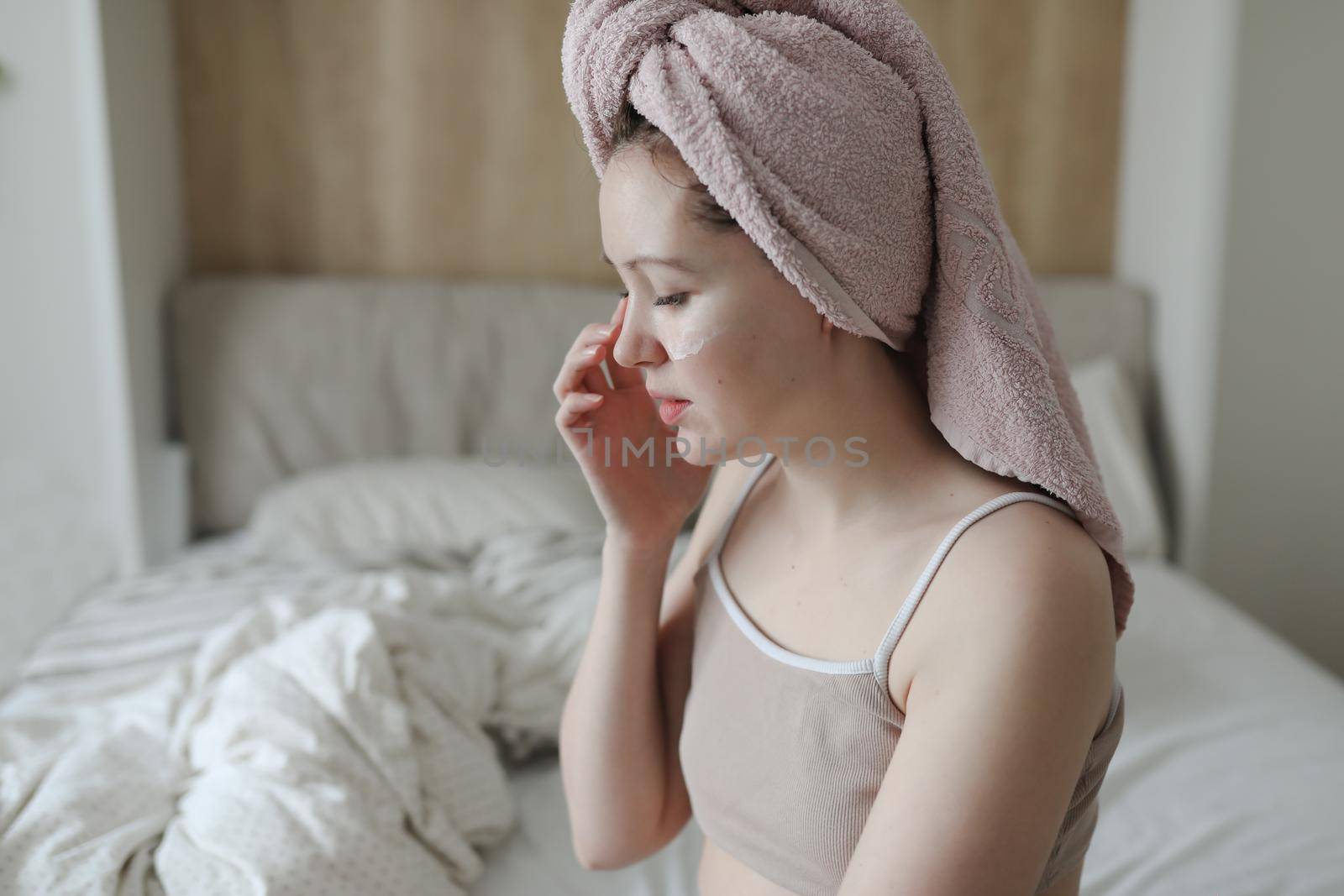 smiling young woman with a towel on head apply cream on face skin