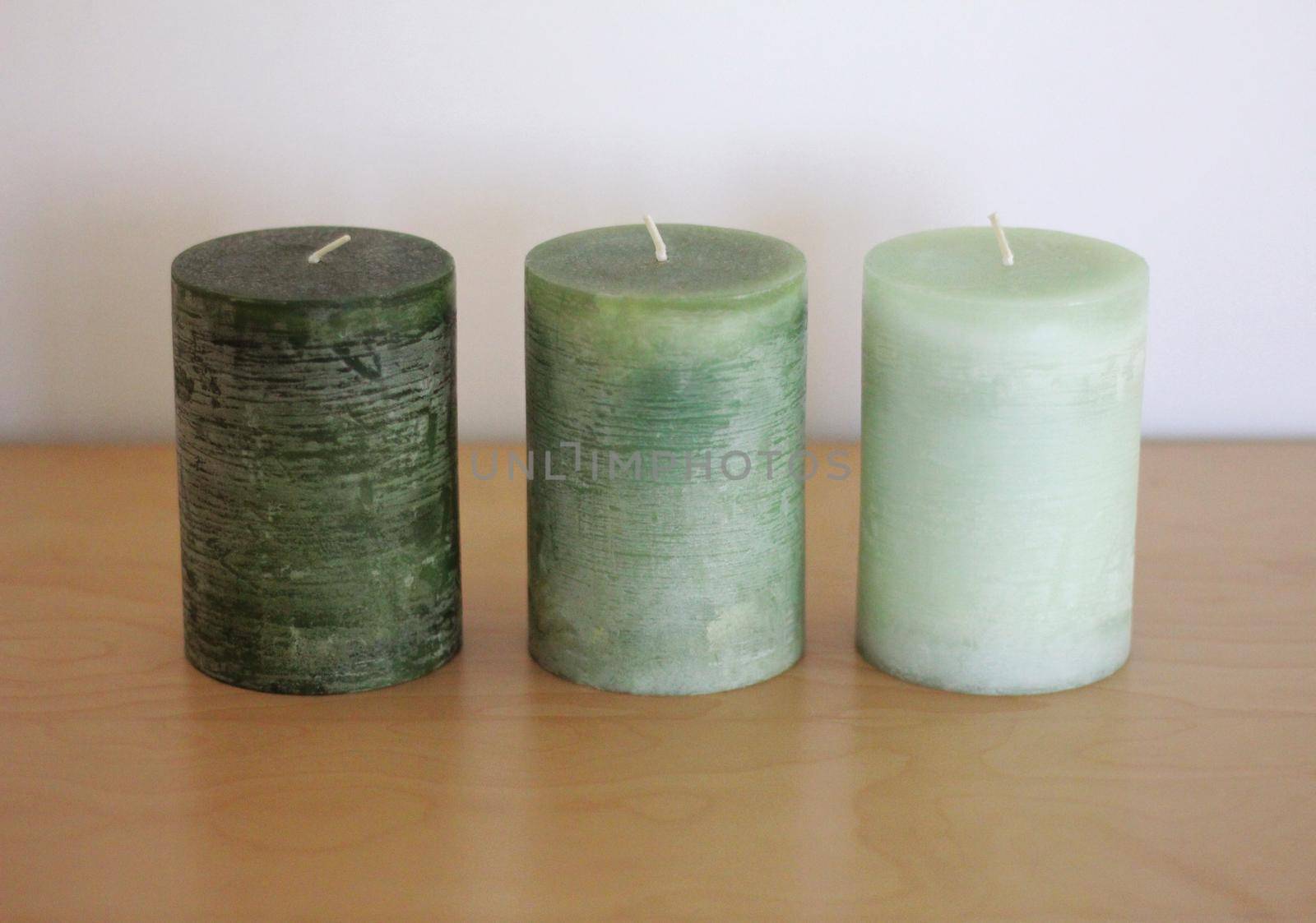 three green aroma candles are standing on a wooden table. the color is changing from dark green to light green