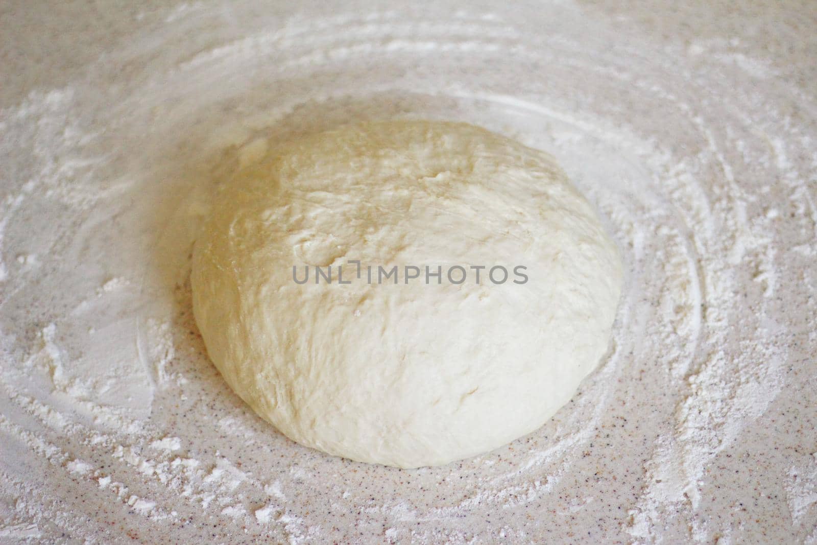 a yeast dough for pizza and bread is on kitchen table. there is a flour around it. the dough is waiting for its time to be baked