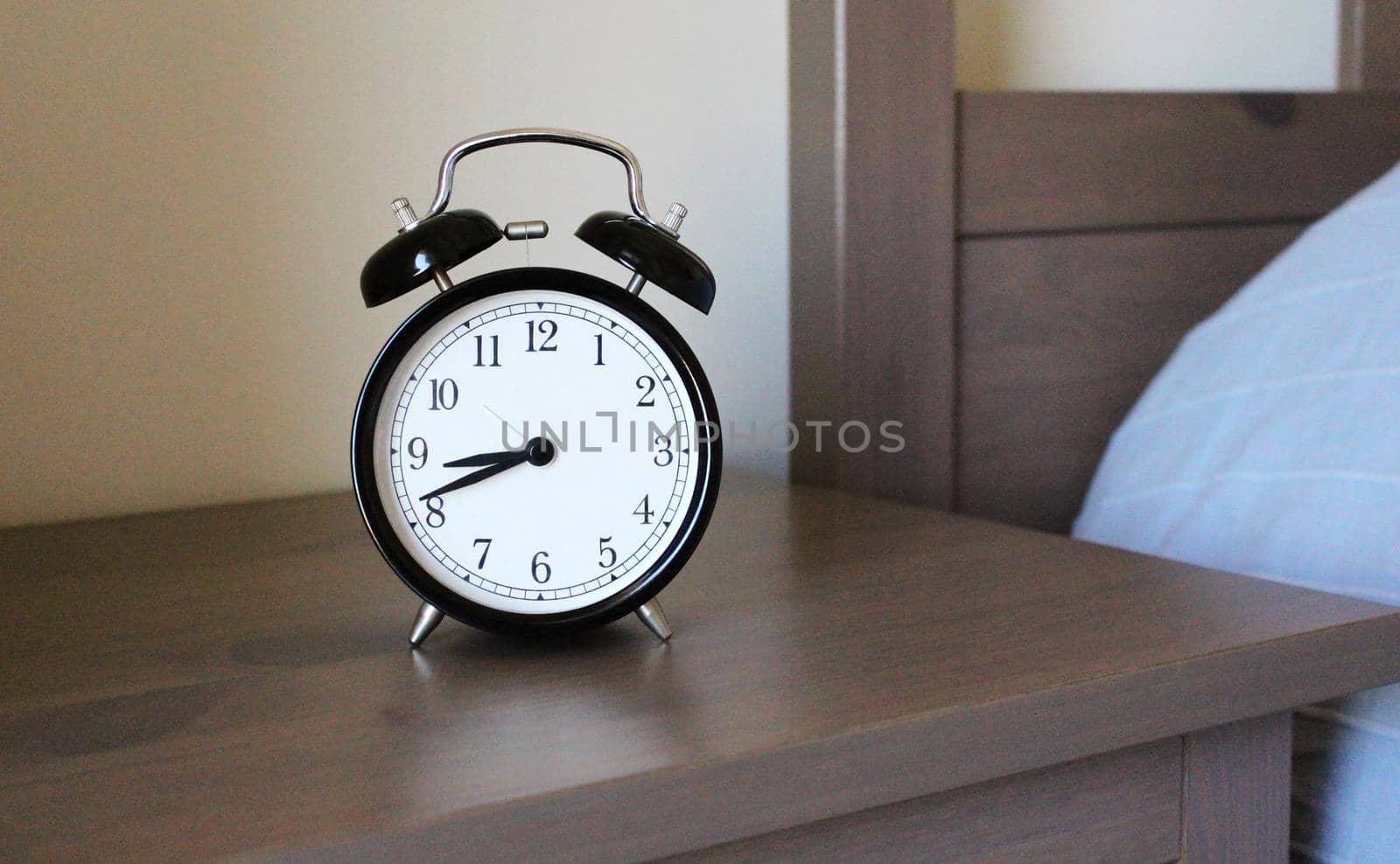 round old metal alarm clock is on a wooden table near a bed. it is 8:42 am. it is time to wake up