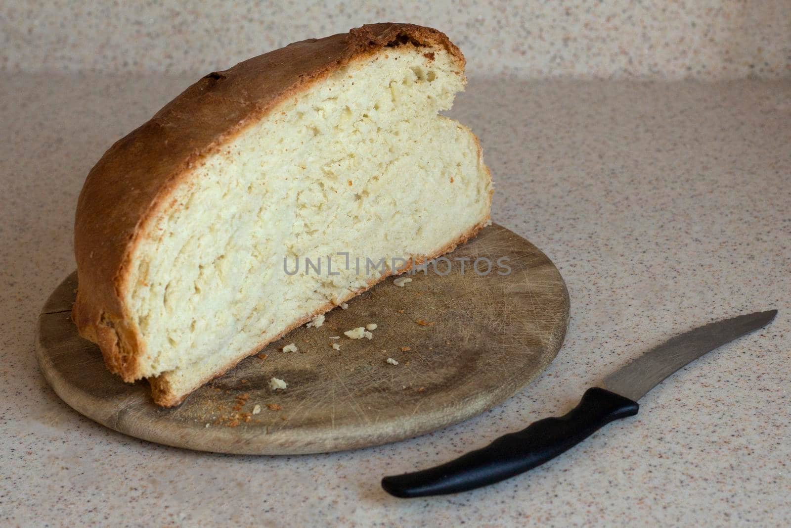 home made fresh bread with crispy crust. it is a half of a loaf is on a kitchen board. there is a knife behind it