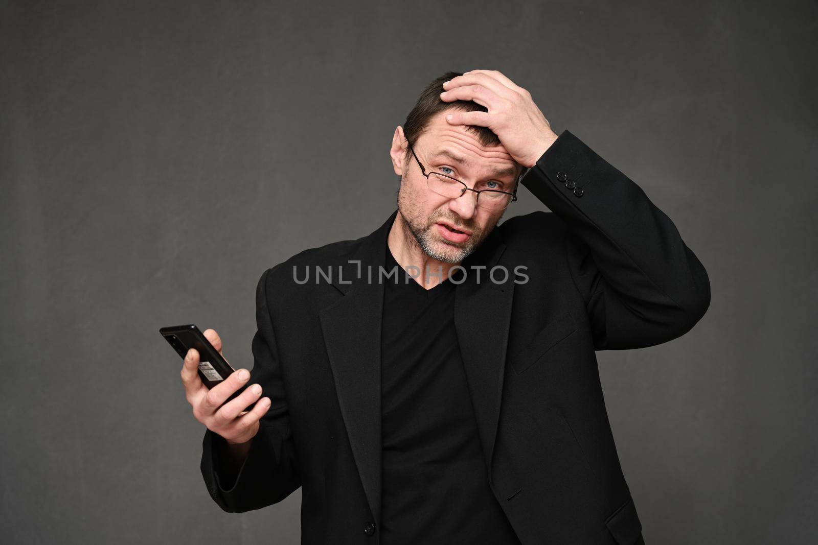 Portrait of a caucasian man in a jacket with an annoyance with a phone in his hands on a gray background