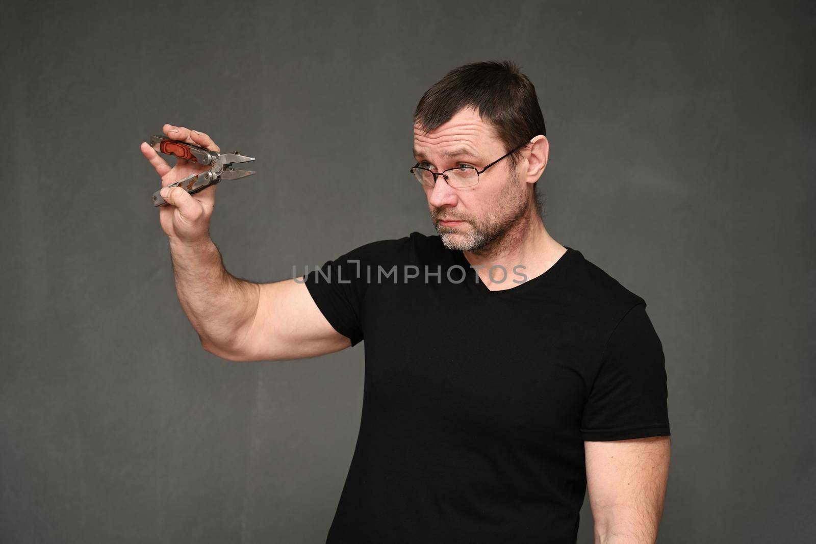 Middle-aged man in a black T-shirt and glasses with pliers in his hands