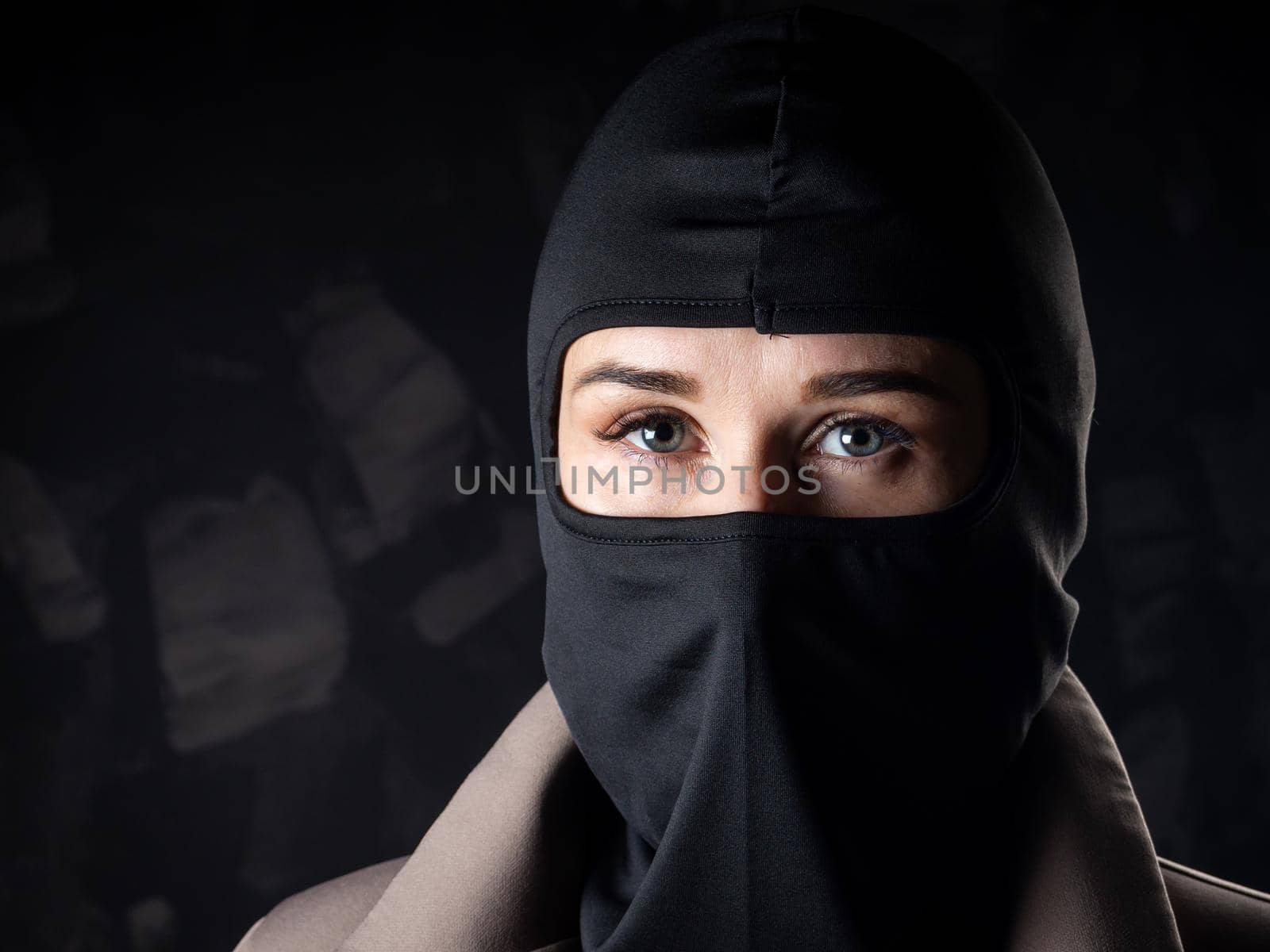 Portrait of a girl in a black balaclava and beige coat. Shot in the studio on a dark background.