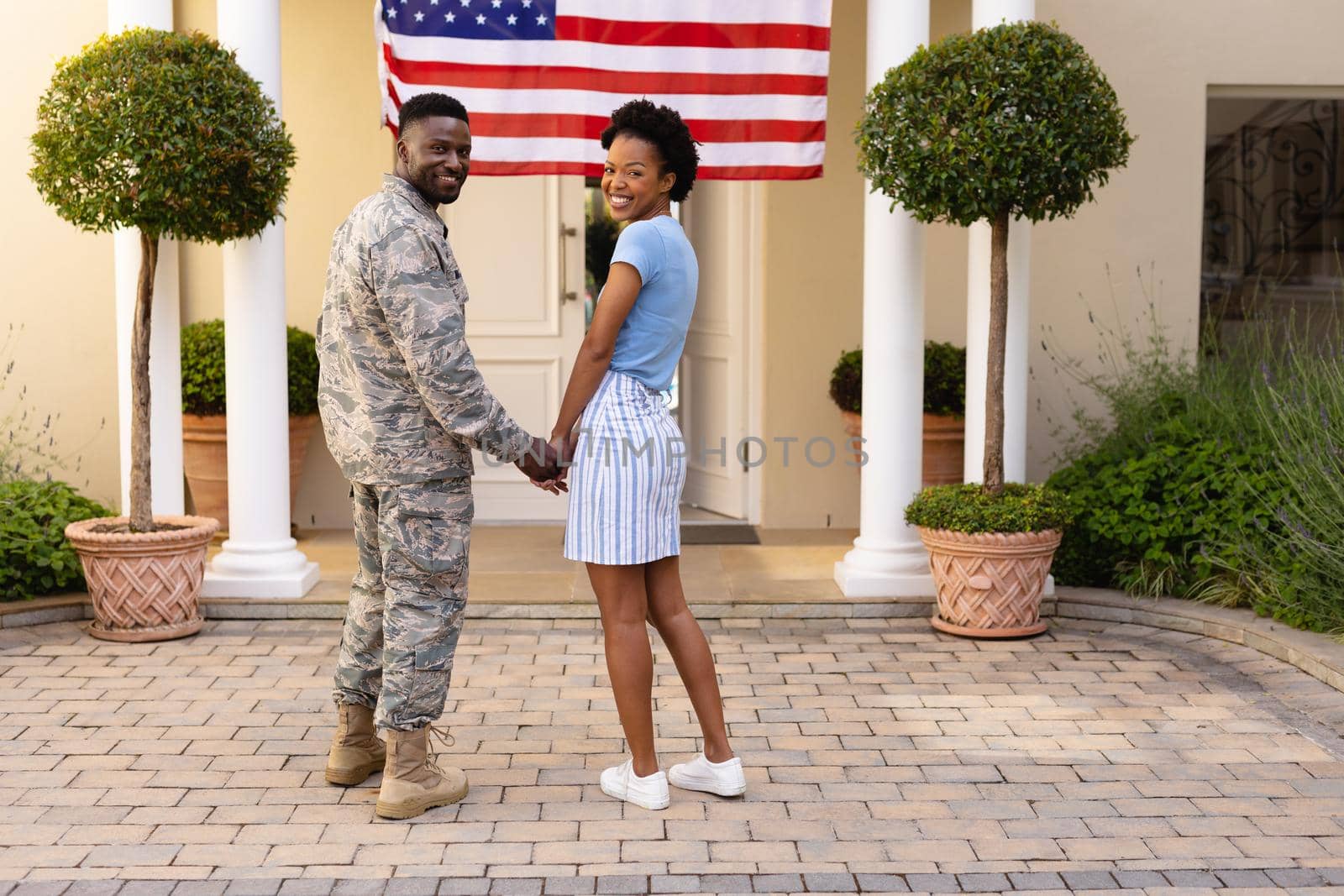 Rear view portrait of smiling african american military man with woman holding hands at entrance. togetherness, bonding and patriotism, unaltered.