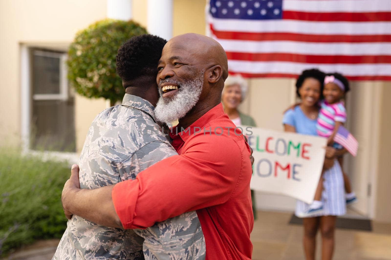 Happy african american senior bald man embracing army soldier against family. bonding and patriotism, unaltered.