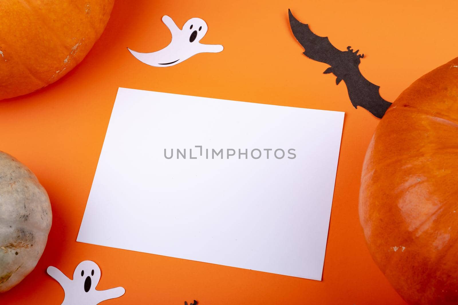Composition of halloween decoration with ghost, bat and sheet with copy space on orange background. halloween tradition and celebration concept digitally generated image.