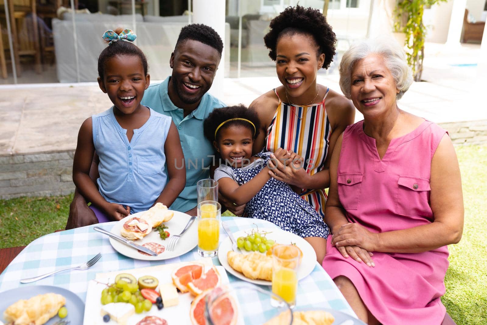 Portrait of smiling african american family sitting at dining table during brunch in backyard. family, love and togetherness concept, unaltered.