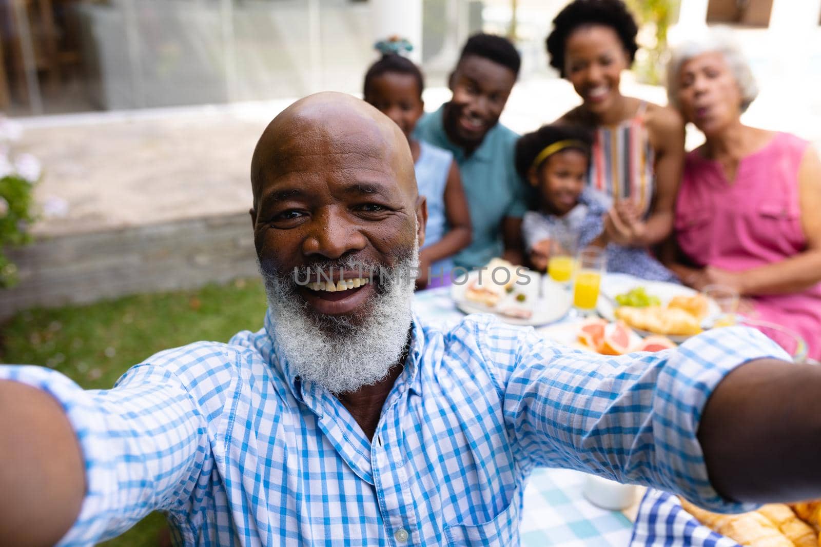 Portrait of smiling bearded bald senior african american man taking selfie with family at brunch by Wavebreakmedia