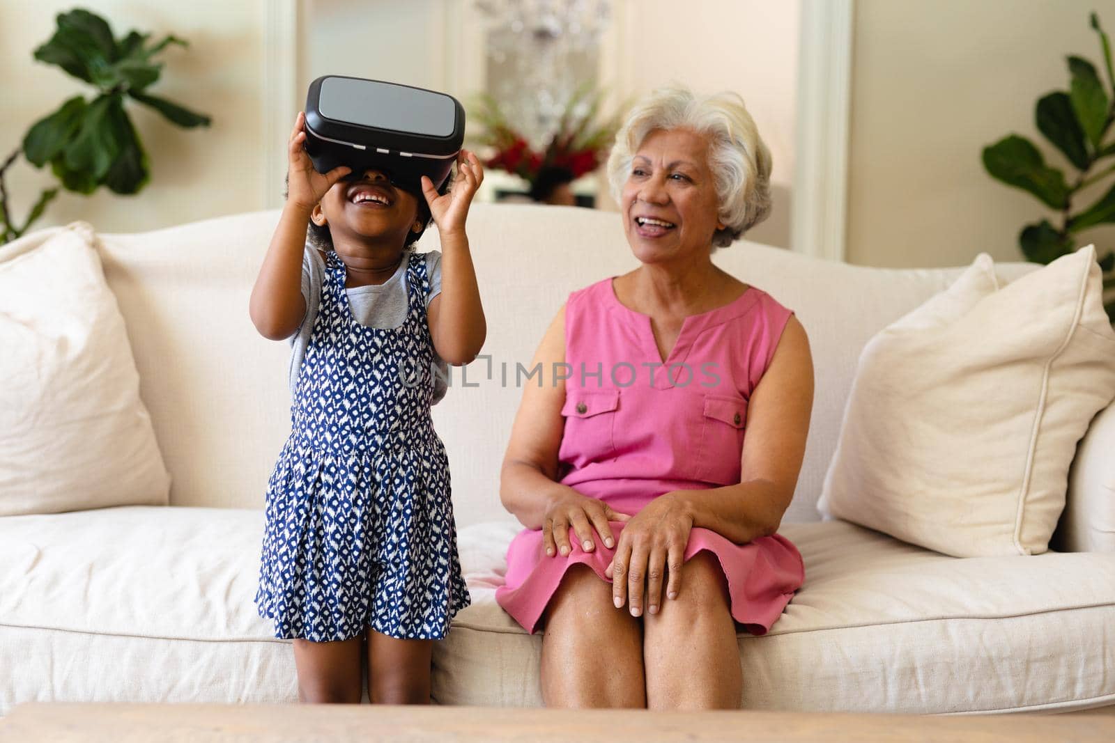 African american girl wearing vr headset and grandmother smiling sitting on the couch by Wavebreakmedia