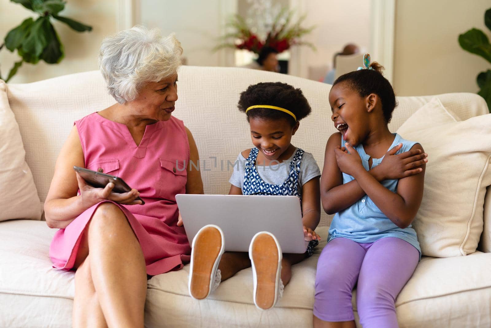 African american grandmother and her two granddaughters using laptop sitting on couch at home by Wavebreakmedia