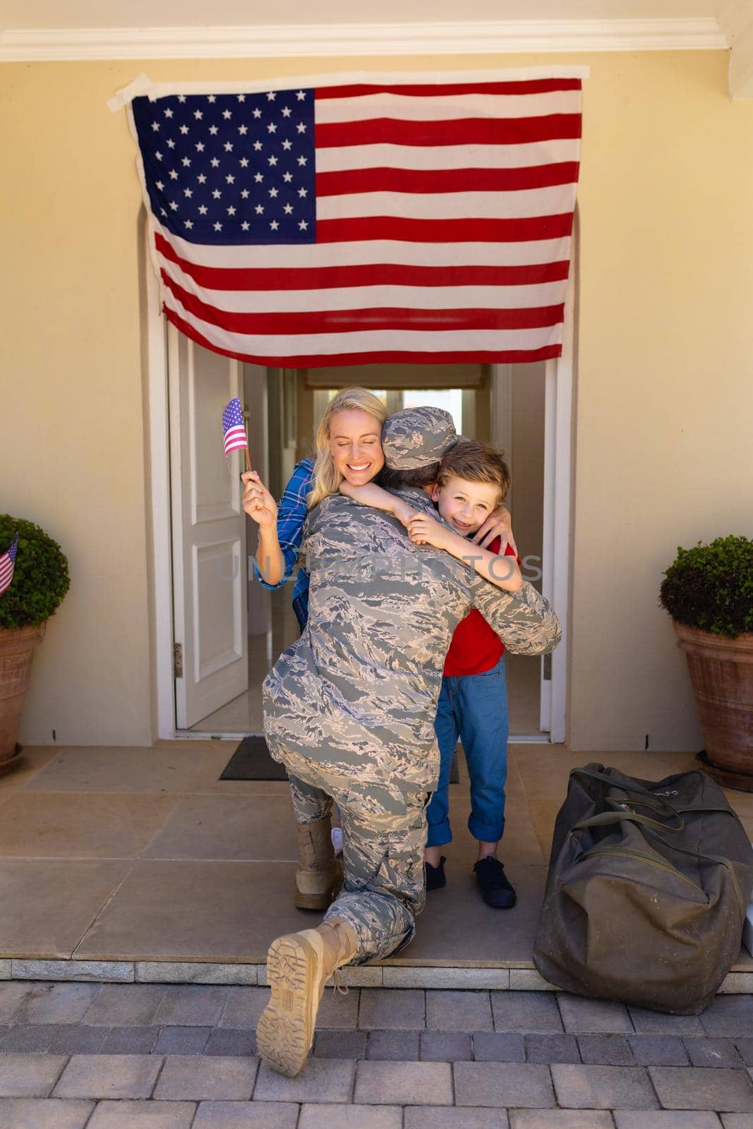 Caucasian woman and son with usa flag hugging army soldier on his return at the entrance by Wavebreakmedia