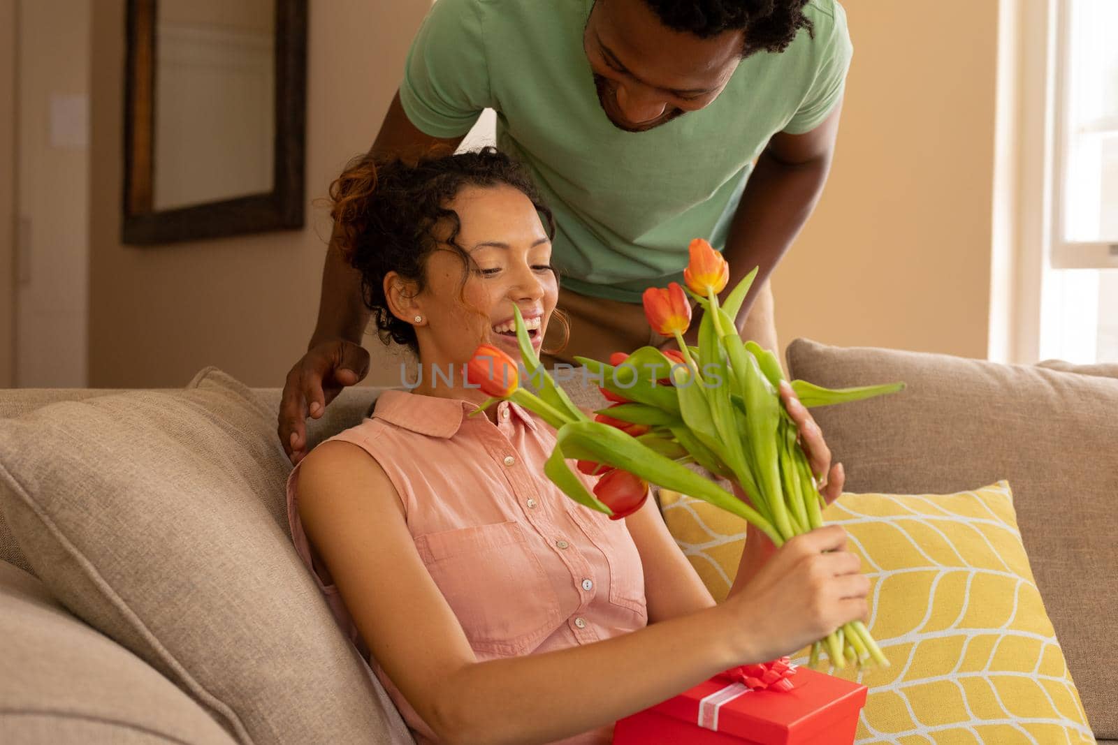 African american man giving tulip flowers and gift to biracial girlfriend on valentine's day at home. love, lifestyle and surprise, unaltered.