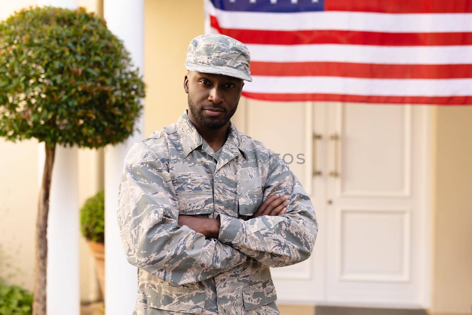 Portrait of confident african american army man in uniform with arms crossed against flag on house by Wavebreakmedia