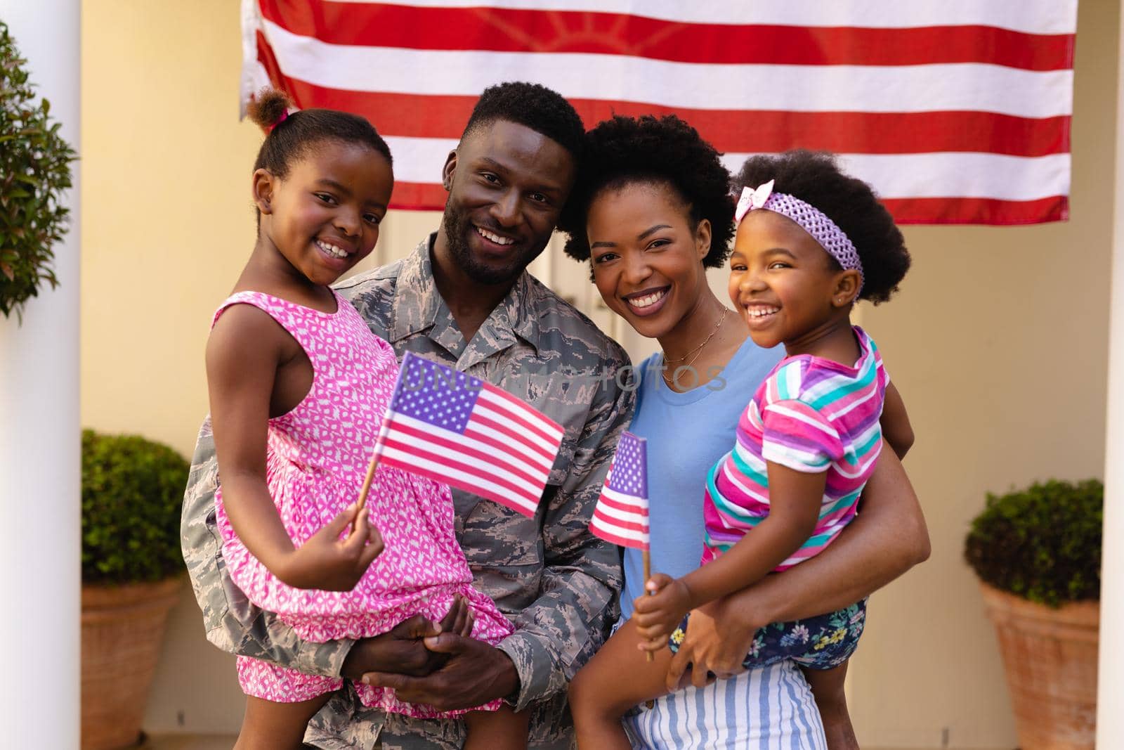 Portrait of smiling african american army soldier and woman carrying daughters at house entrance. family, bonding and patriotism, unaltered.