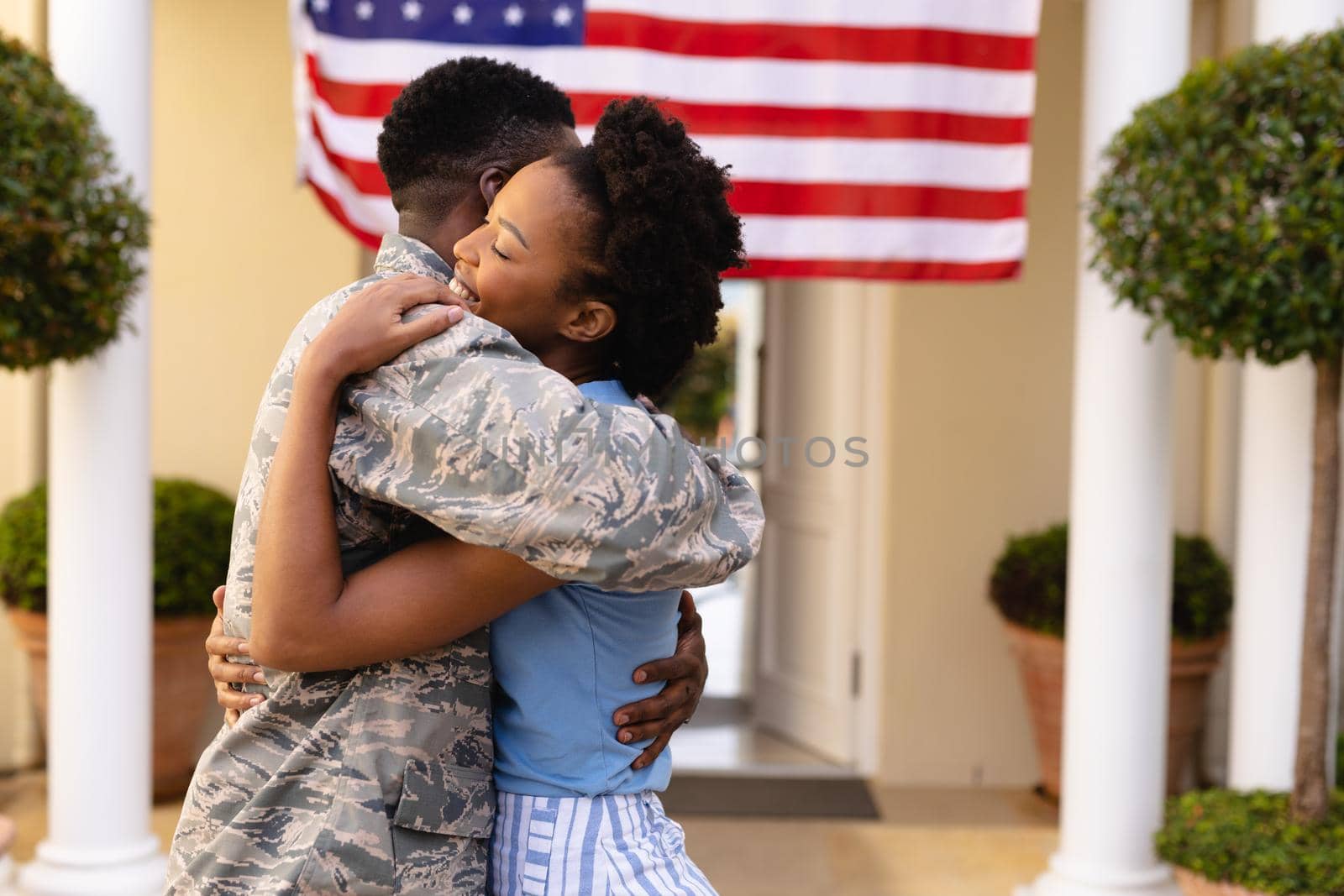 Side view of happy african american woman embracing military soldier at house entrance. togetherness, bonding and patriotism, unaltered.