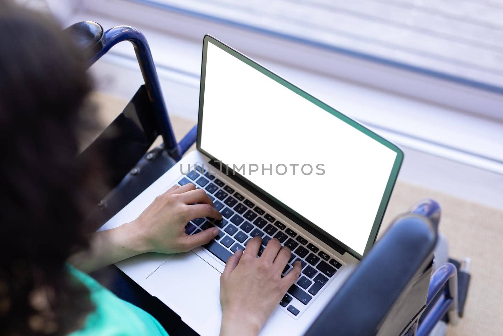 High angle view of biracial disabled woman on wheelchair using laptop with copy space on blank. technology and disability, unaltered.