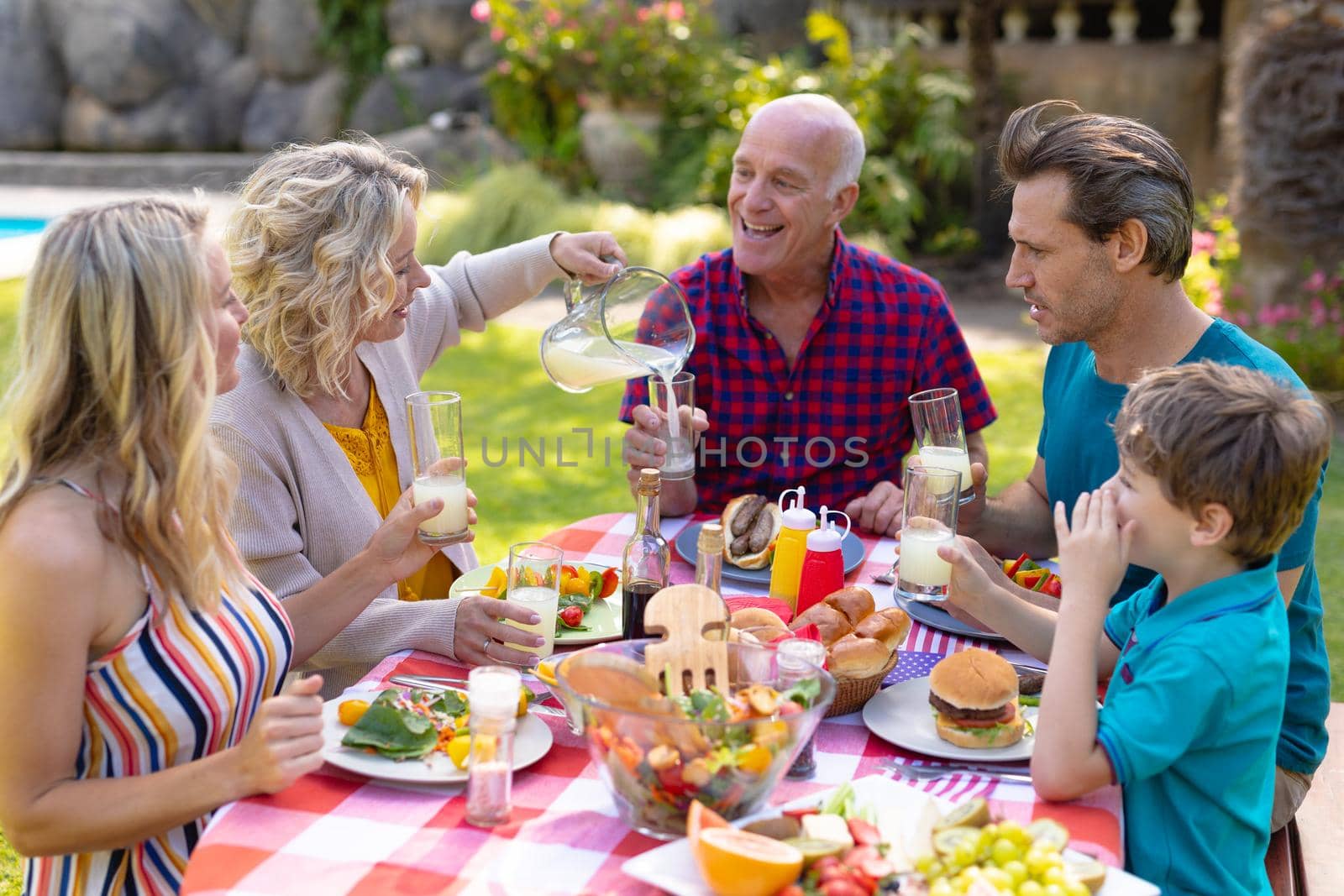 Cheerful caucasian three generational family enjoying lunch at table in garden. family, togetherness and weekend lifestyle concept, unaltered.