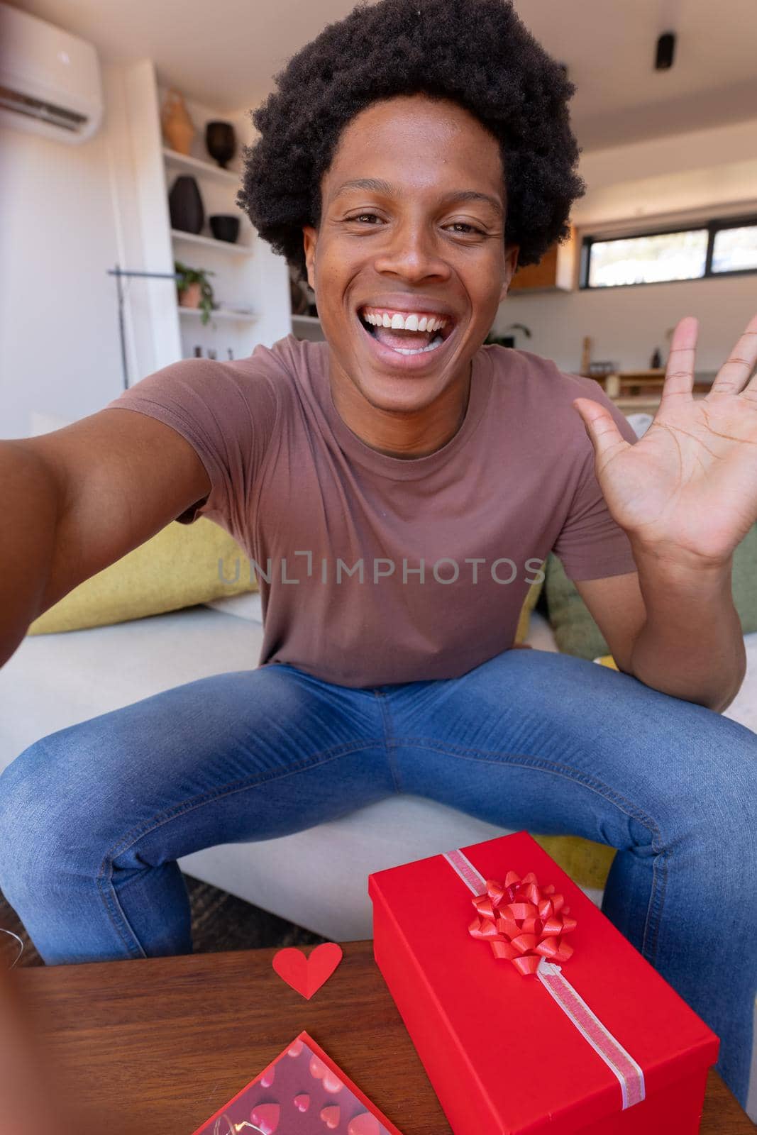 Portrait of cheerful african american young man waving during video call while sitting at home by Wavebreakmedia