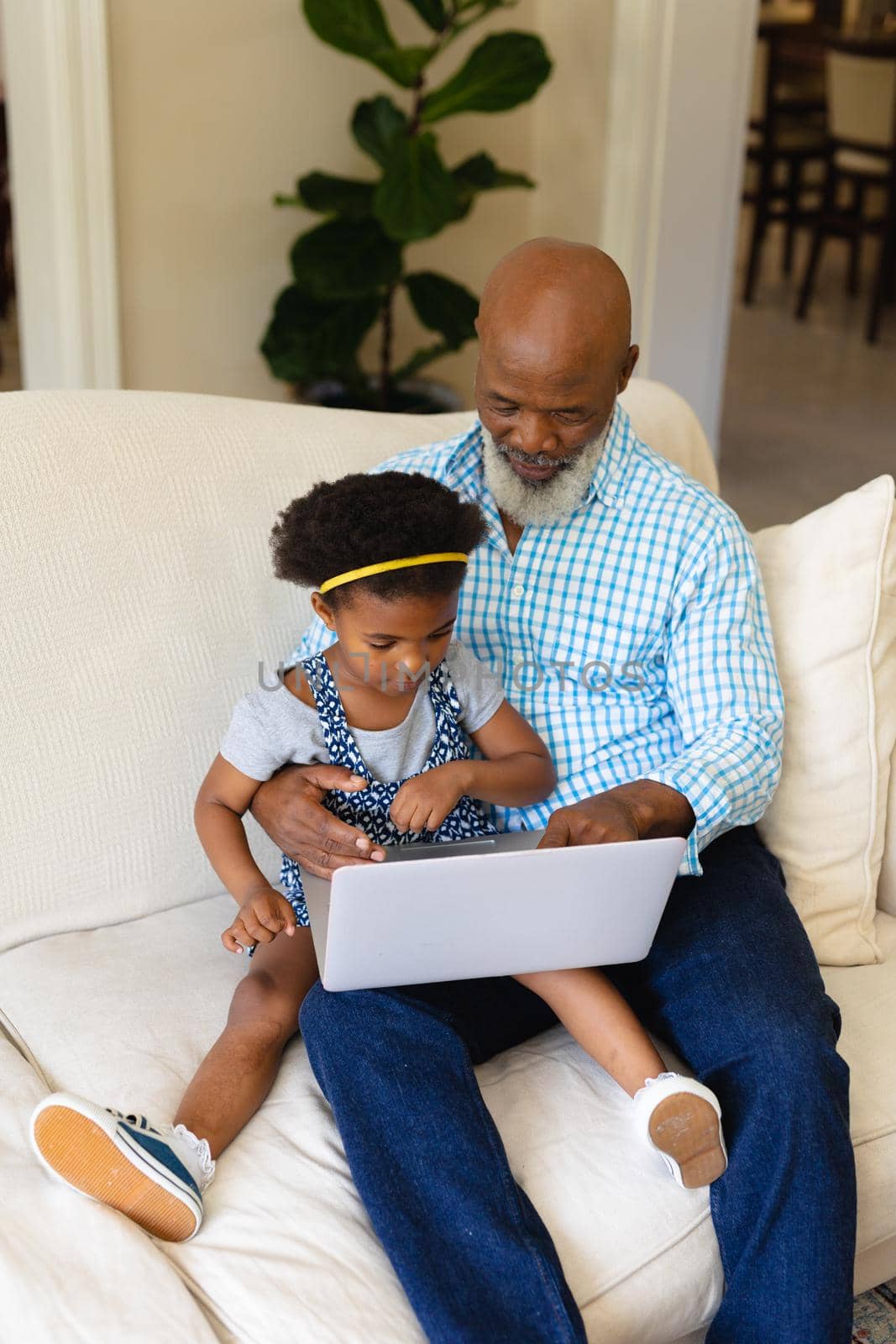 African american grandfather and his granddaughter using laptop together sitting on couch at home. family, love and technology concept, unaltered.