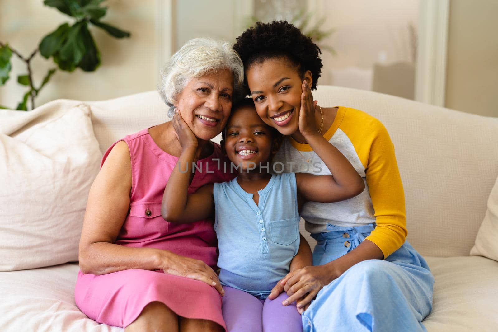 Portrait of african american grandmother, mother and granddaughter smiling sitting on couch at home. family, love and togetherness concept, unaltered.