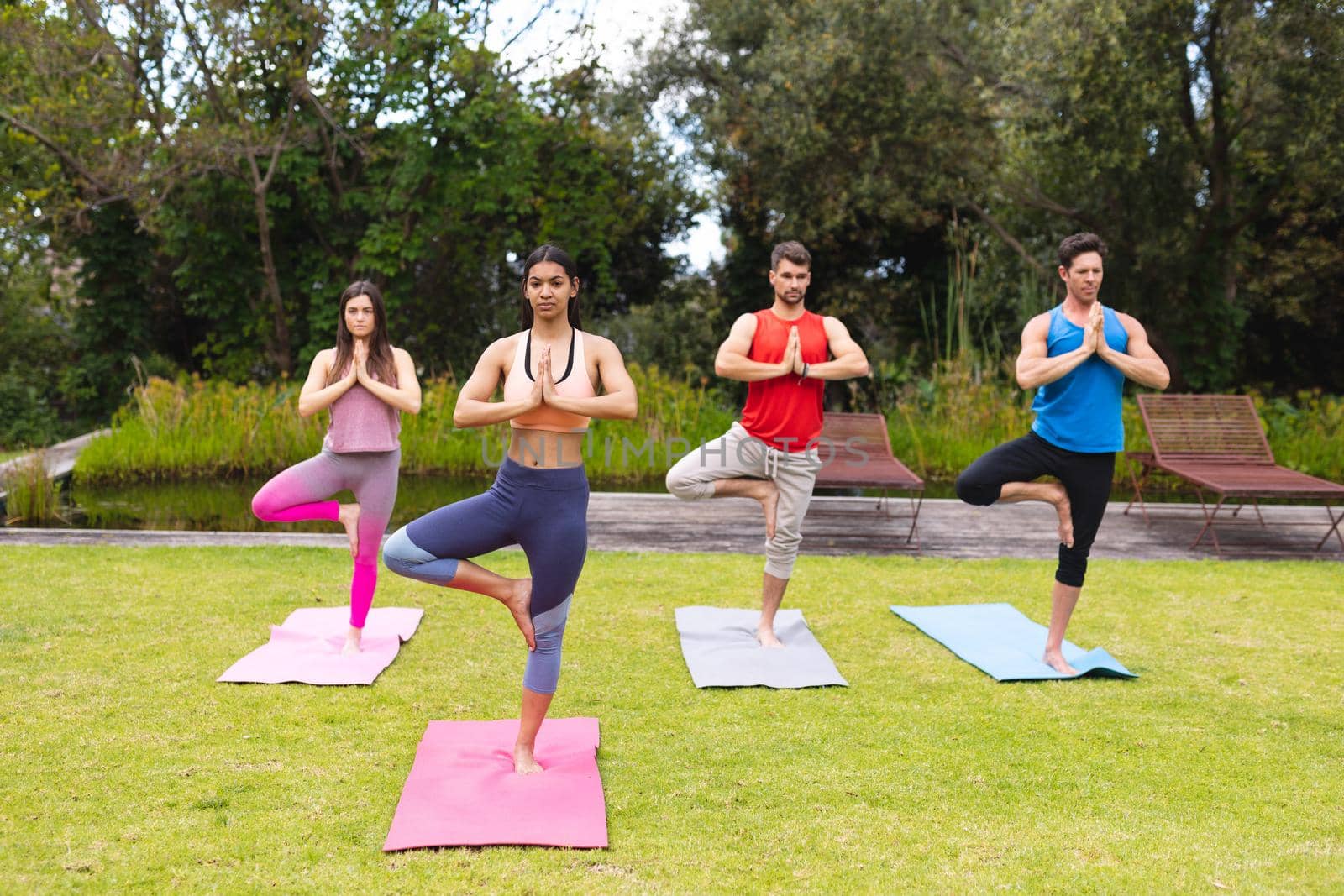 Female instructor teaching tree pose to men and woman on exercise mats during yoga session in park. healthy lifestyle and body care.