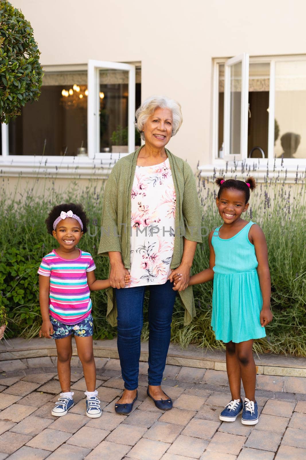 Portrait of african american grandmother holding hands of her granddaughters and smiling outdoors. family, love and togetherness concept, unaltered.