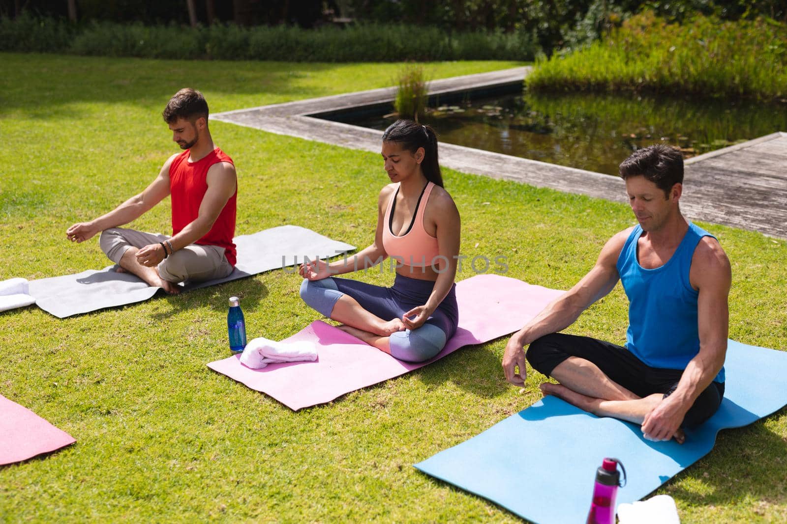 Men and woman in sportswear meditating on exercise mats in park. yoga, healthy lifestyle and body care.