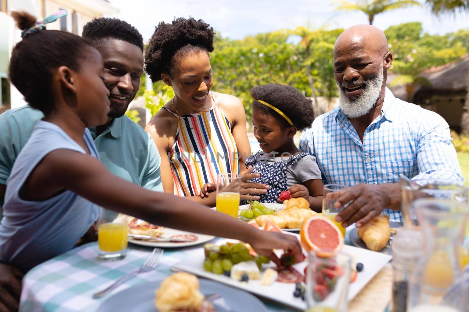 Happy african american family eating brunch at dining table in backyard. family, love and togetherness concept, unaltered.