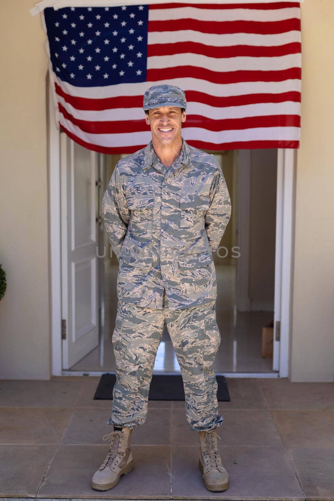 Full length portrait of smiling caucasian army soldier standing against usa flag at entrance. people, patriotism and identity concept, unaltered.
