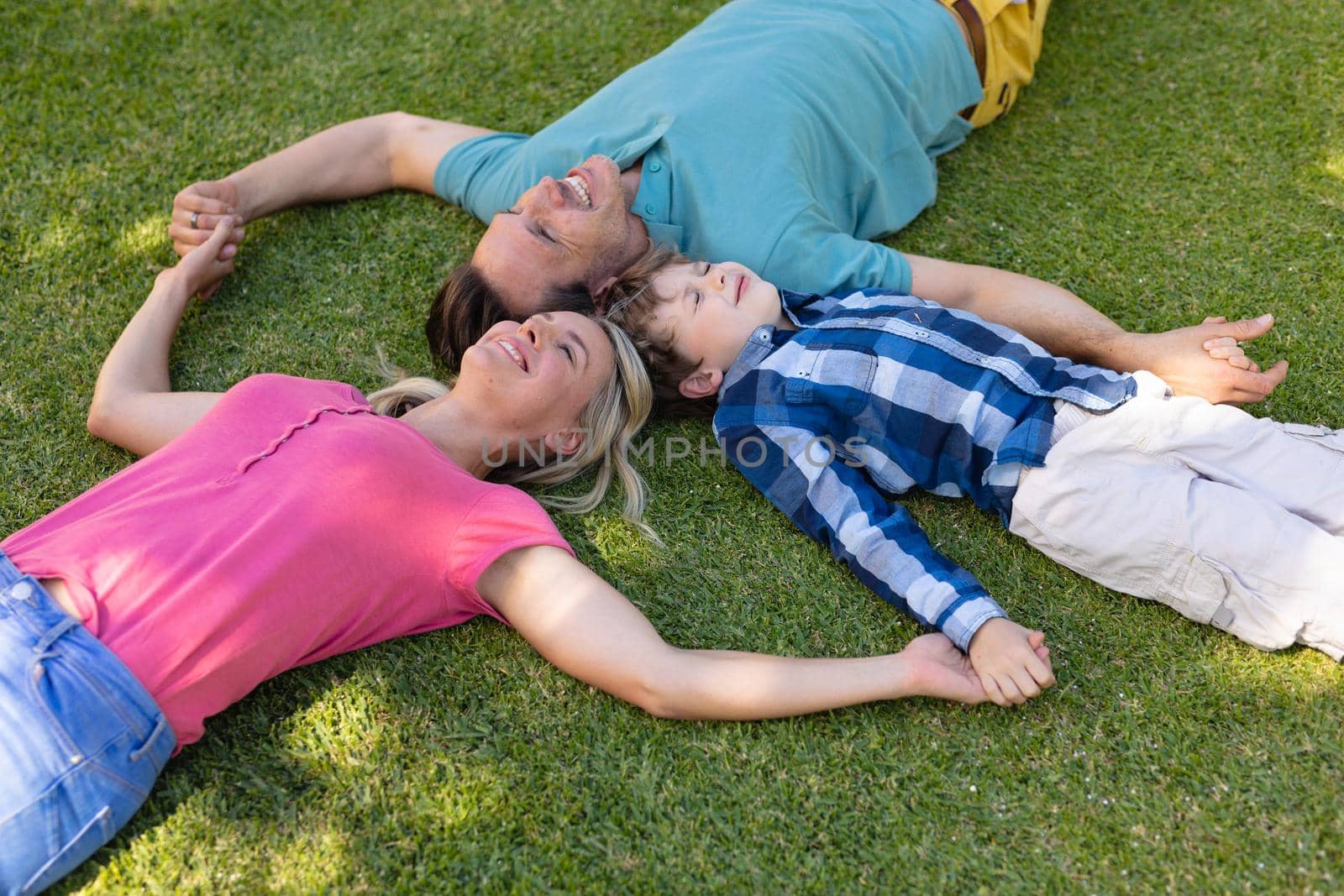 High angle view of caucasian family holding hands and lying together in the garden by Wavebreakmedia