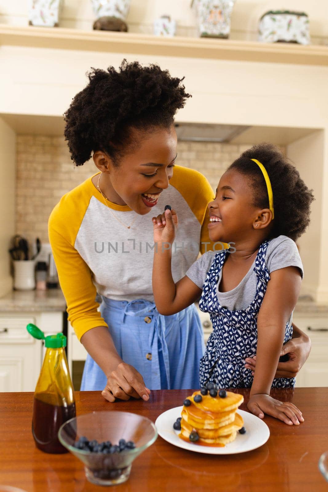 African american daughter feeding berries to her mother in the kitchen at home. family, love and togetherness concept, unaltered.