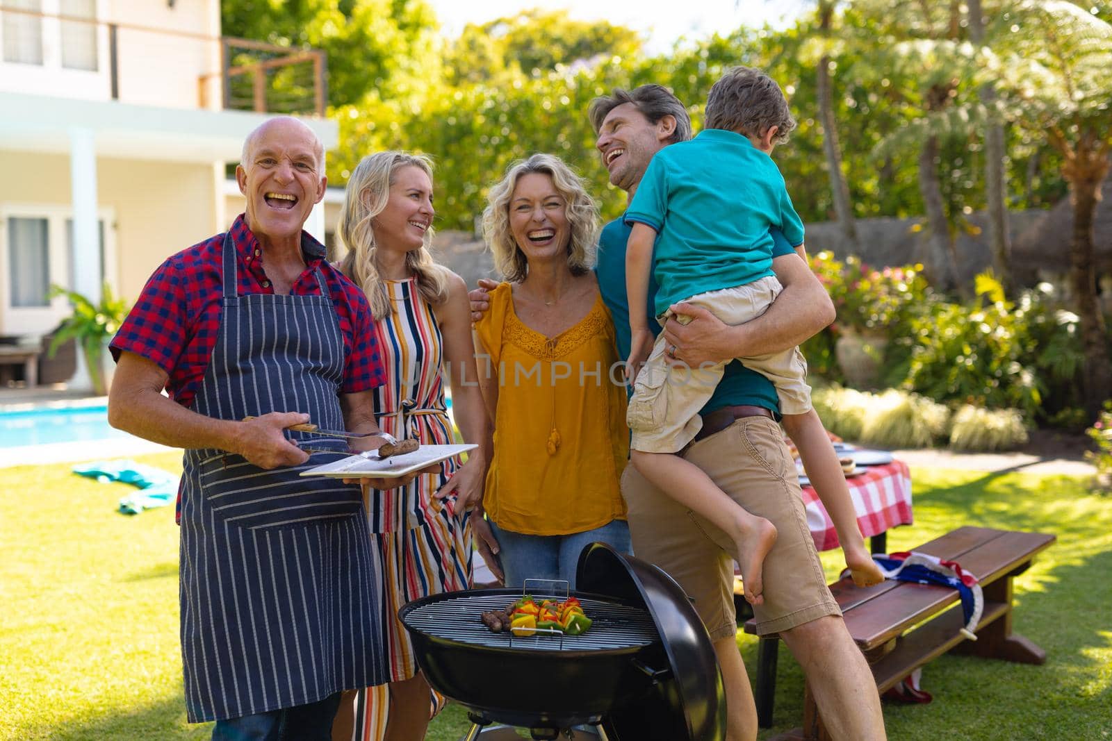 Portrait of cheerful caucasian three generational family barbecuing together in the garden. family, togetherness and weekend lifestyle concept, unaltered.