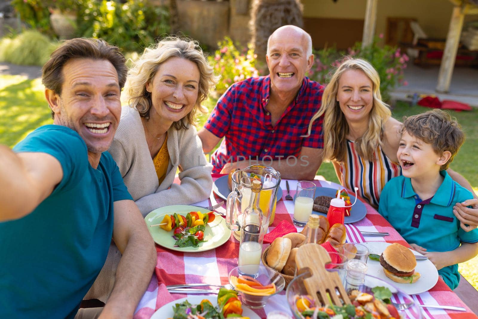 Portrait of cheerful caucasian family taking selfie at table in the garden. family, togetherness and weekend lifestyle concept, unaltered.