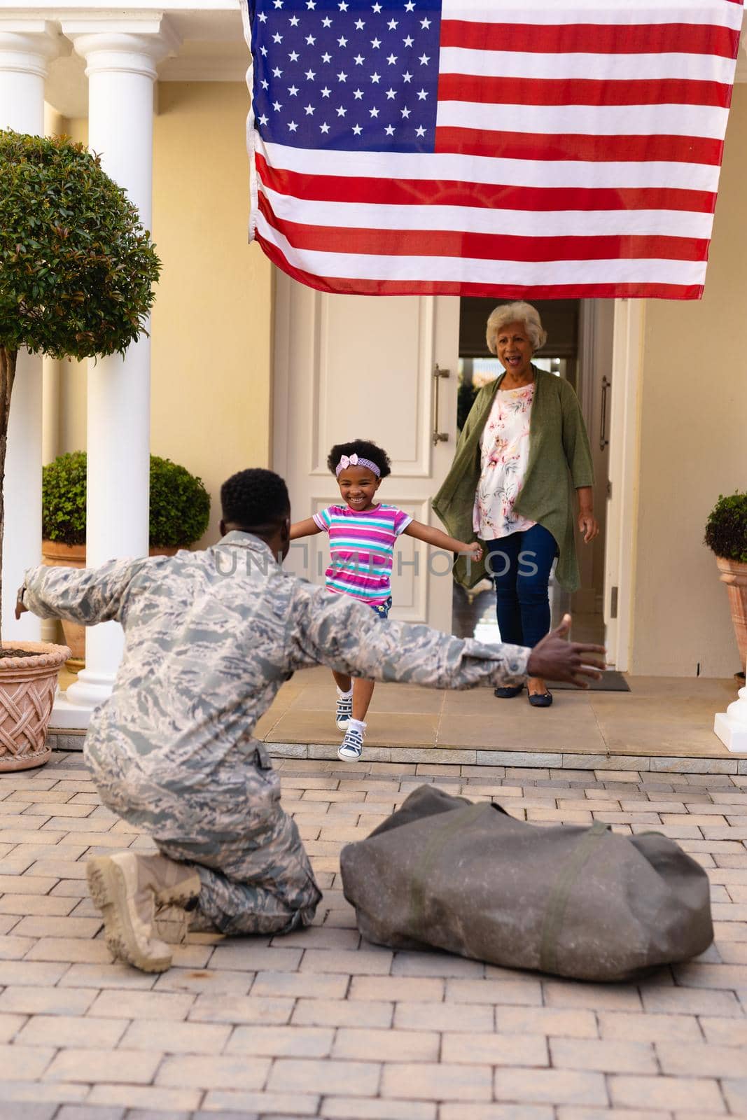 Happy african american girl running towards soldier father returning home with granny at entrance. family, bonding and patriotism, unaltered.